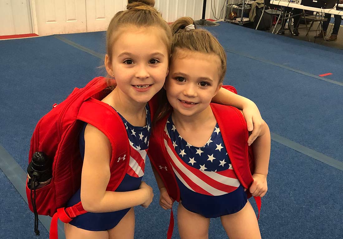 two gymnasts hugging each other with backpacks on
